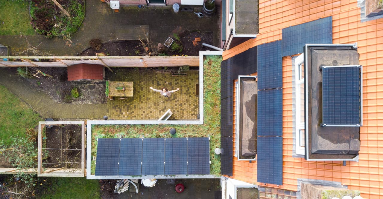 Hoge drone foto, vrouw onderin met armen gespreid, alle zonnepanelen in beeld.