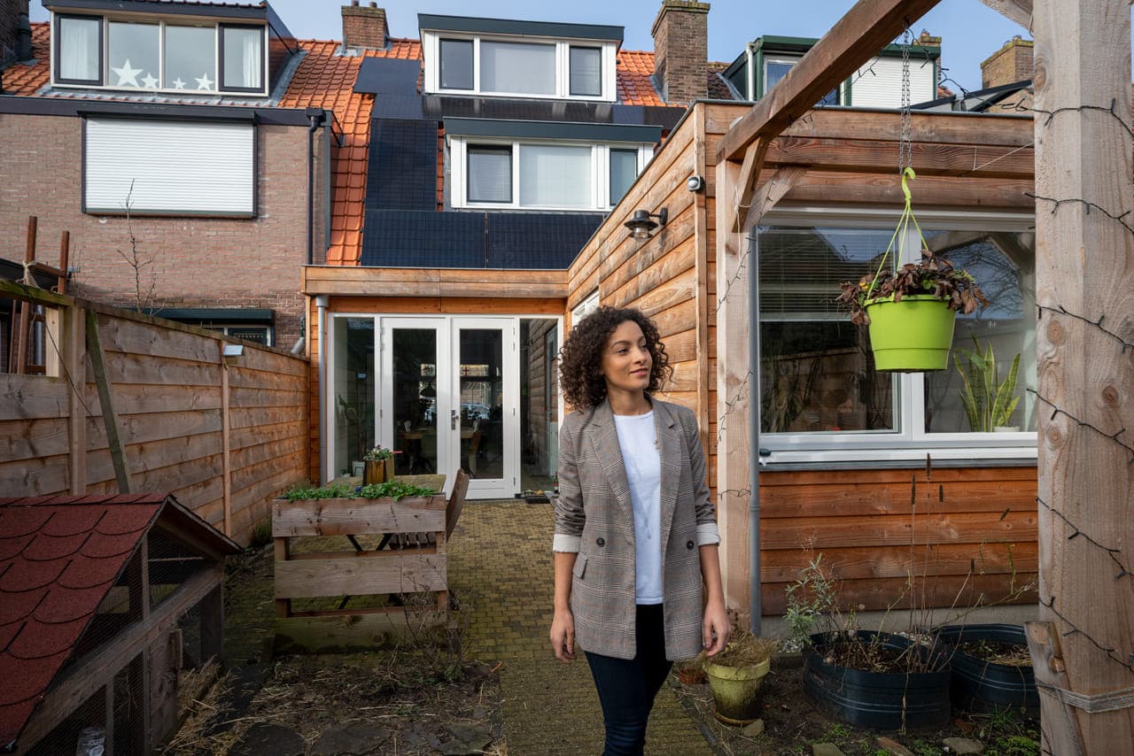 Vrouw in achtertuin, huis op achtergrond bijna in beeld, zonnepanelen in beeld.