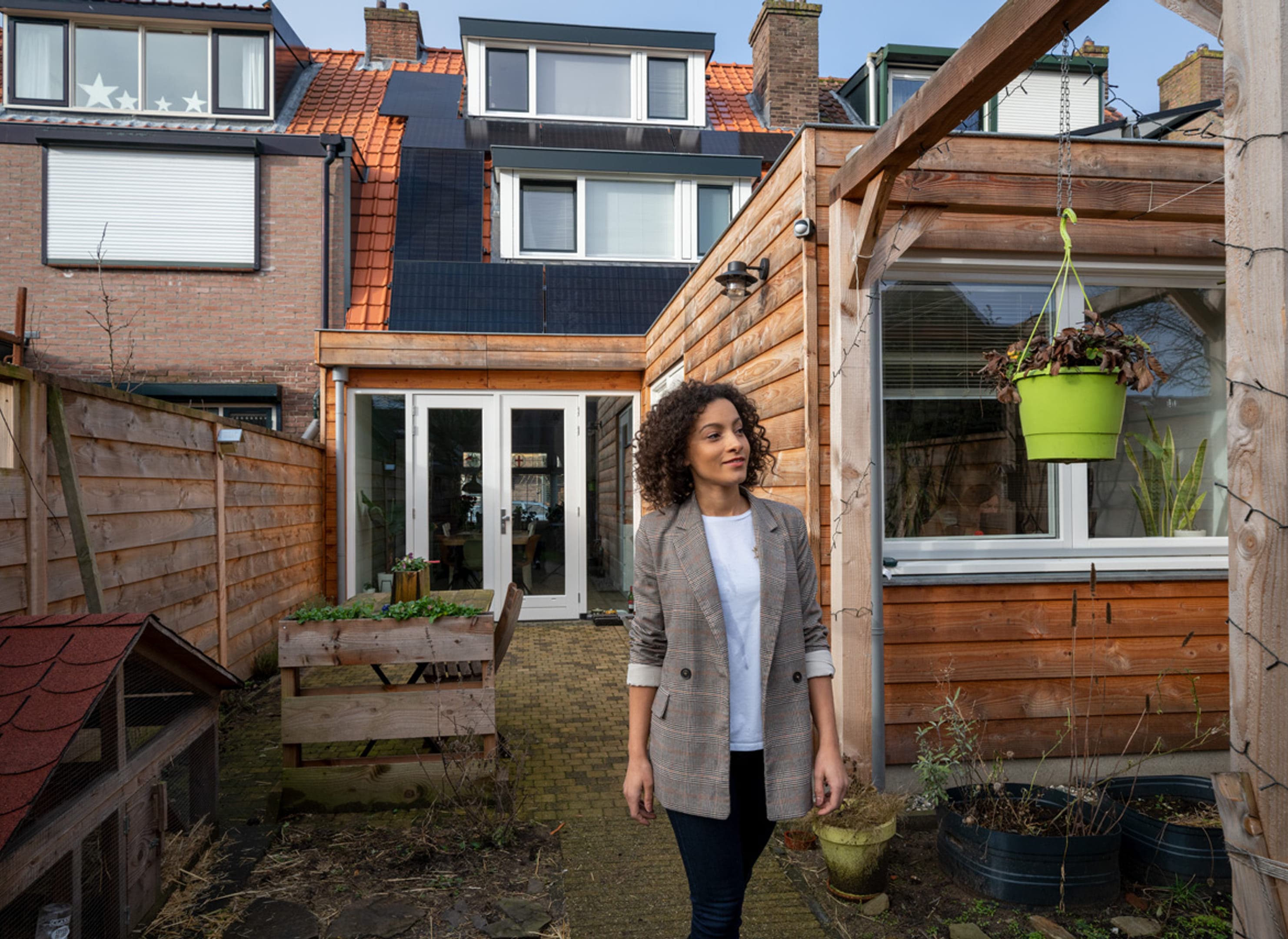 Vrouw in achtertuin, huis op achtergrond bijna in beeld, zonnepanelen in beeld.