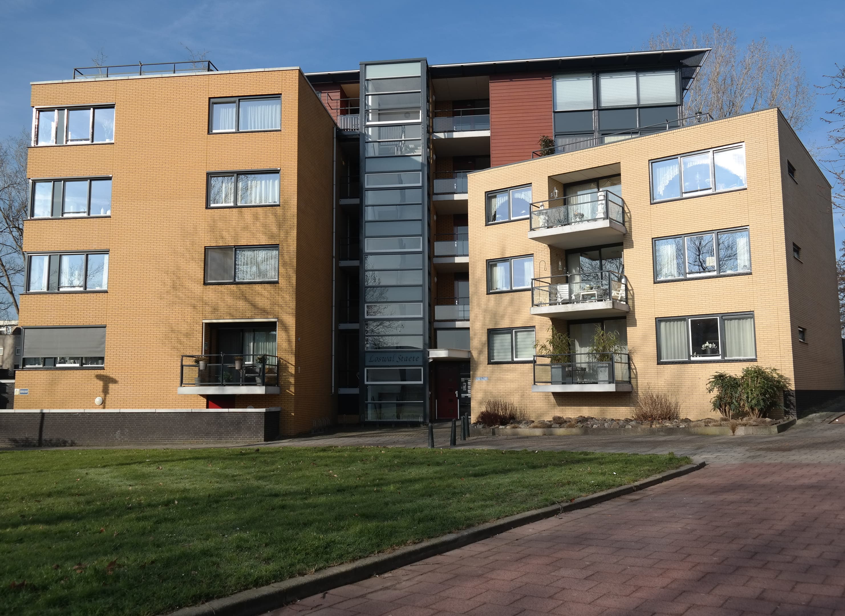 Foto van een appartementengebouw van geel baksteen bestaande uit twee delen.