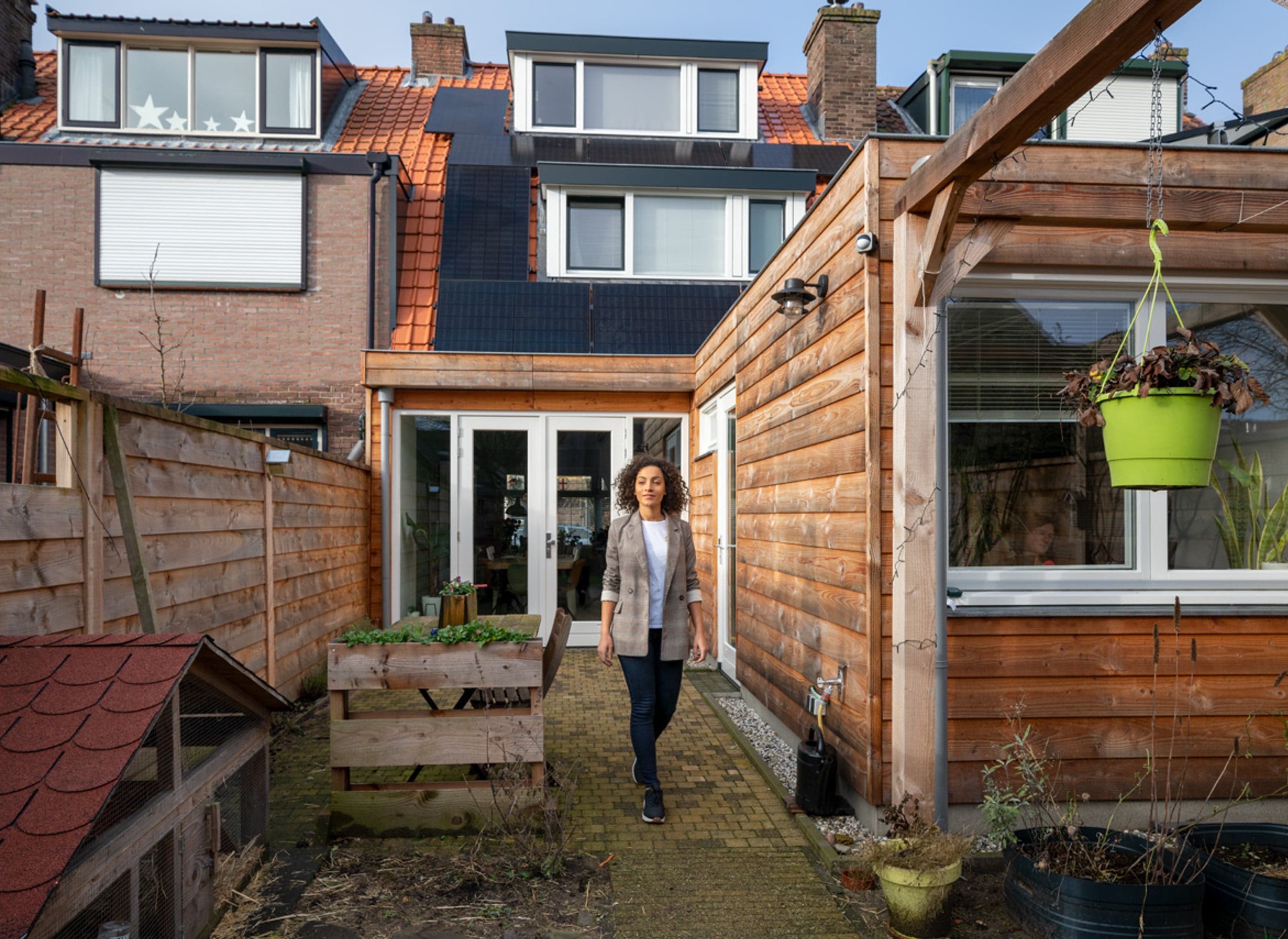 Vrouw in achtertuin, huis op achtergrond bijna in beeld, zonnepanelen in beeld.