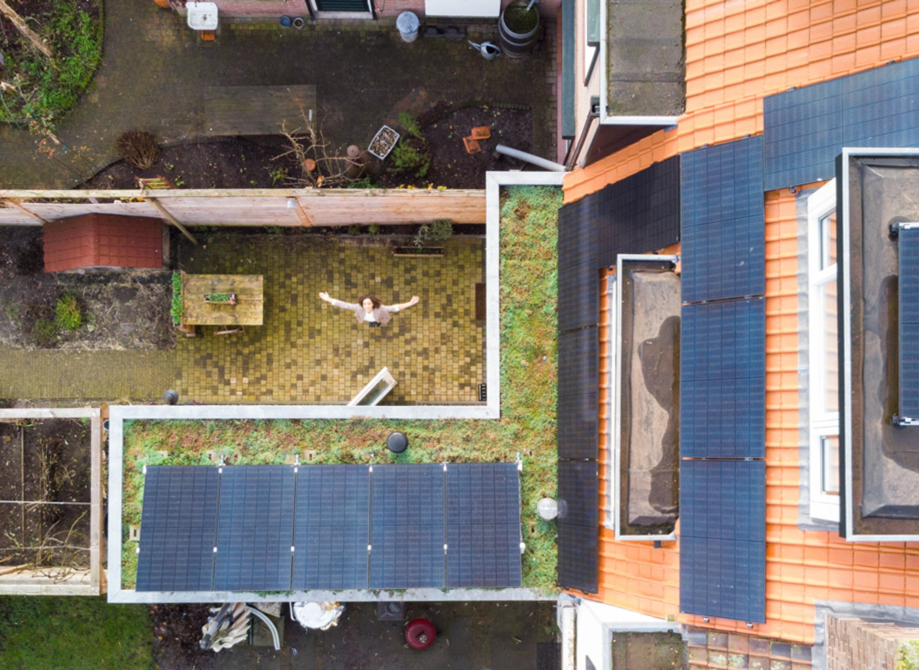 Hoge drone foto, vrouw onderin met armen gespreid, alle zonnepanelen in beeld.