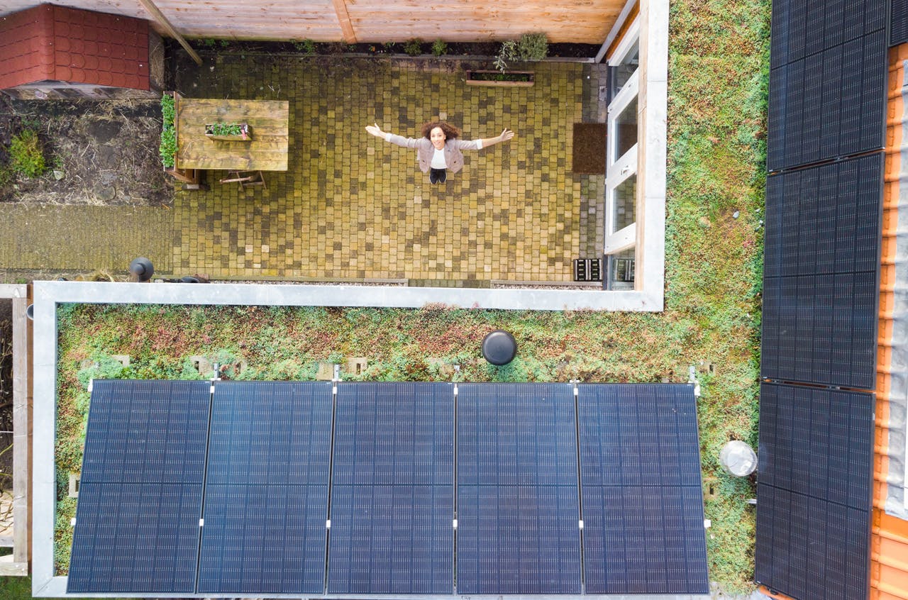 Foto met drone, bovenaf, dakbedekking groen, met zonnepanelen, vrouw in beeld armen gespreid, vorm omgekeerde l.