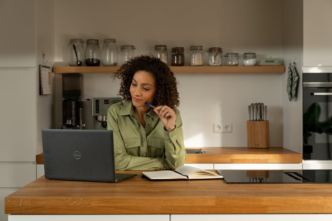 Vrouw in keuken, notitieblok, Dell laptop, koffiemachine op achtergrond.