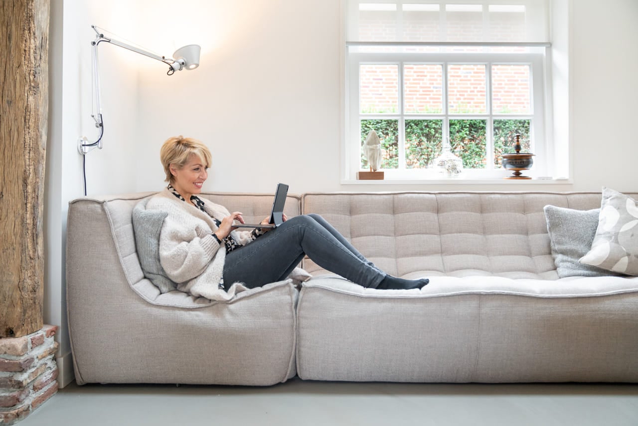 Vrouw relaxed op bank met iPad, van iets verder weg bekeken.