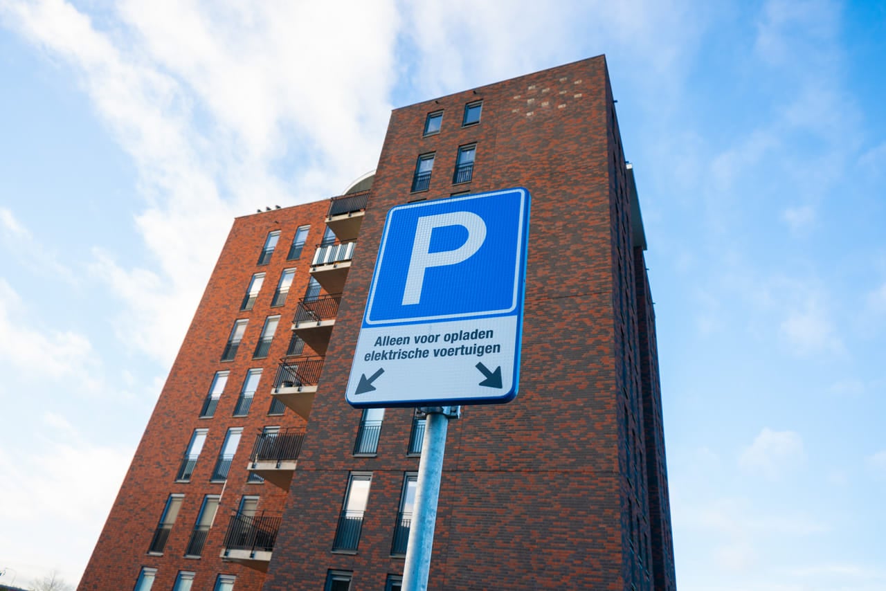 Modern vierkant appartementencomplex met vanuit kikvorsperspectief een parkeerplaats voor laadpalen.