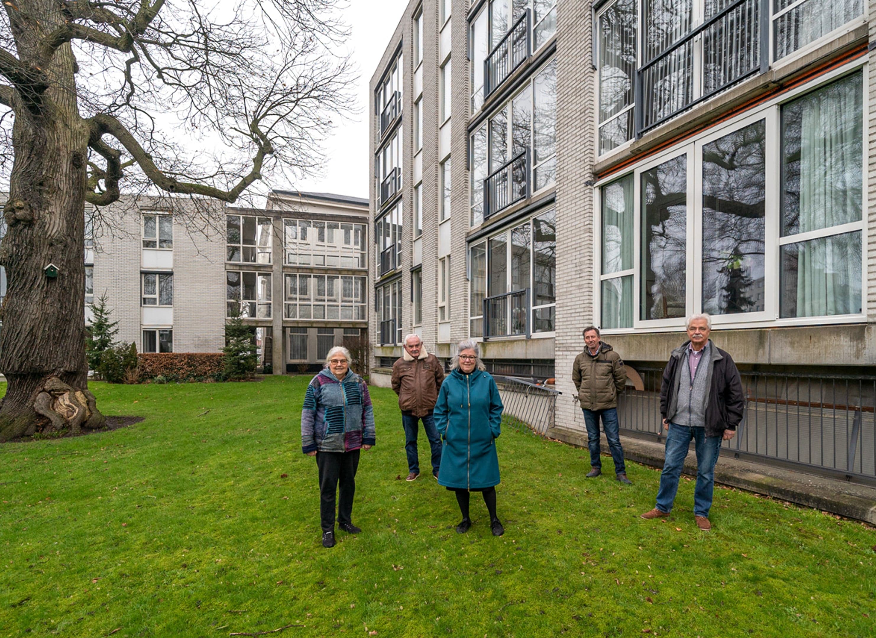 Vijf mensen bij een appartementengebouw, moderne bouw met lichte bakstenen