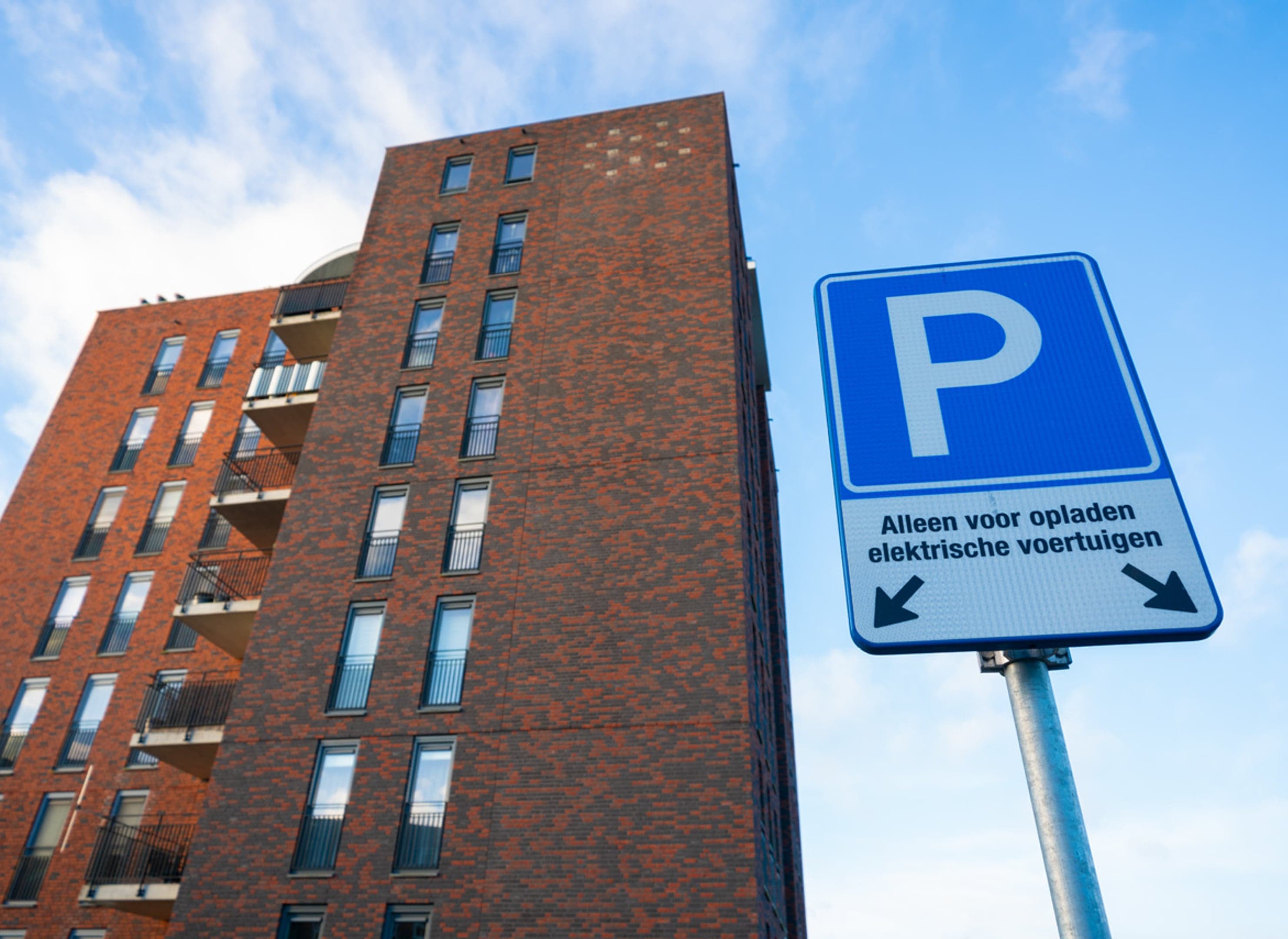 Modern vierkant appartementsgebouw, rode baksteen, met op de voorgrond een Parkeerbord alleen voor elektrische voertuigen