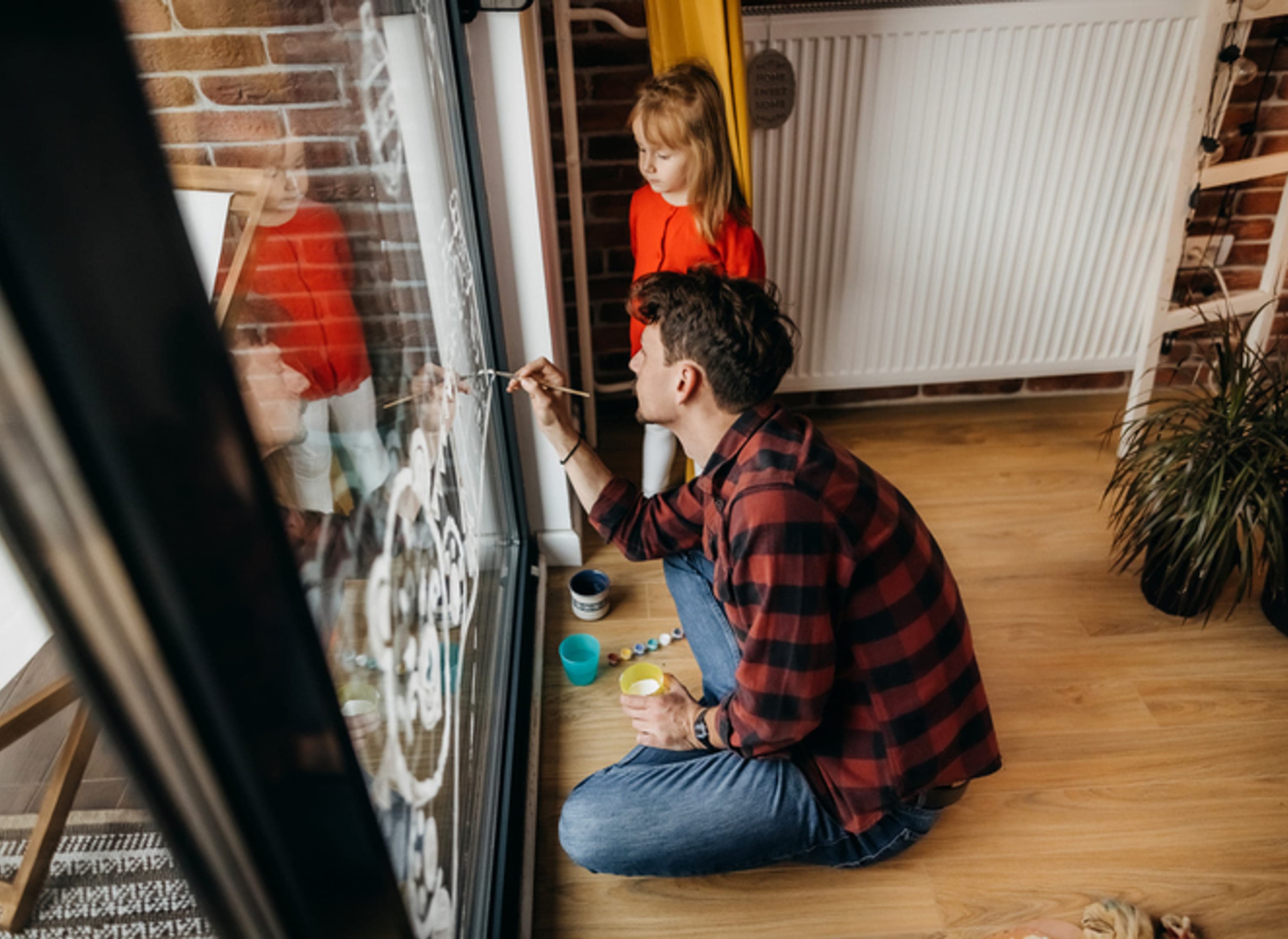 Man verft tekening op een raam, kind staat ernaast en kijkt