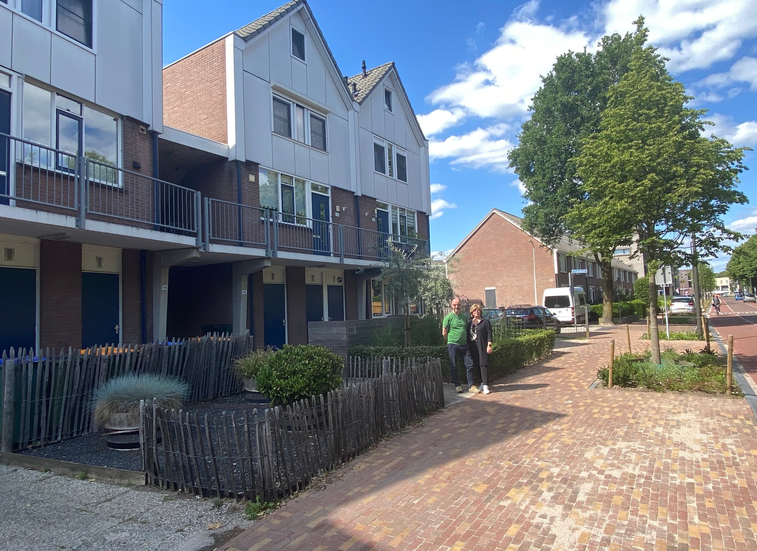 Rijtjeshuizen met puntdak, vier verdiepingen, en een echtpaar bij de ingang van hun tuin