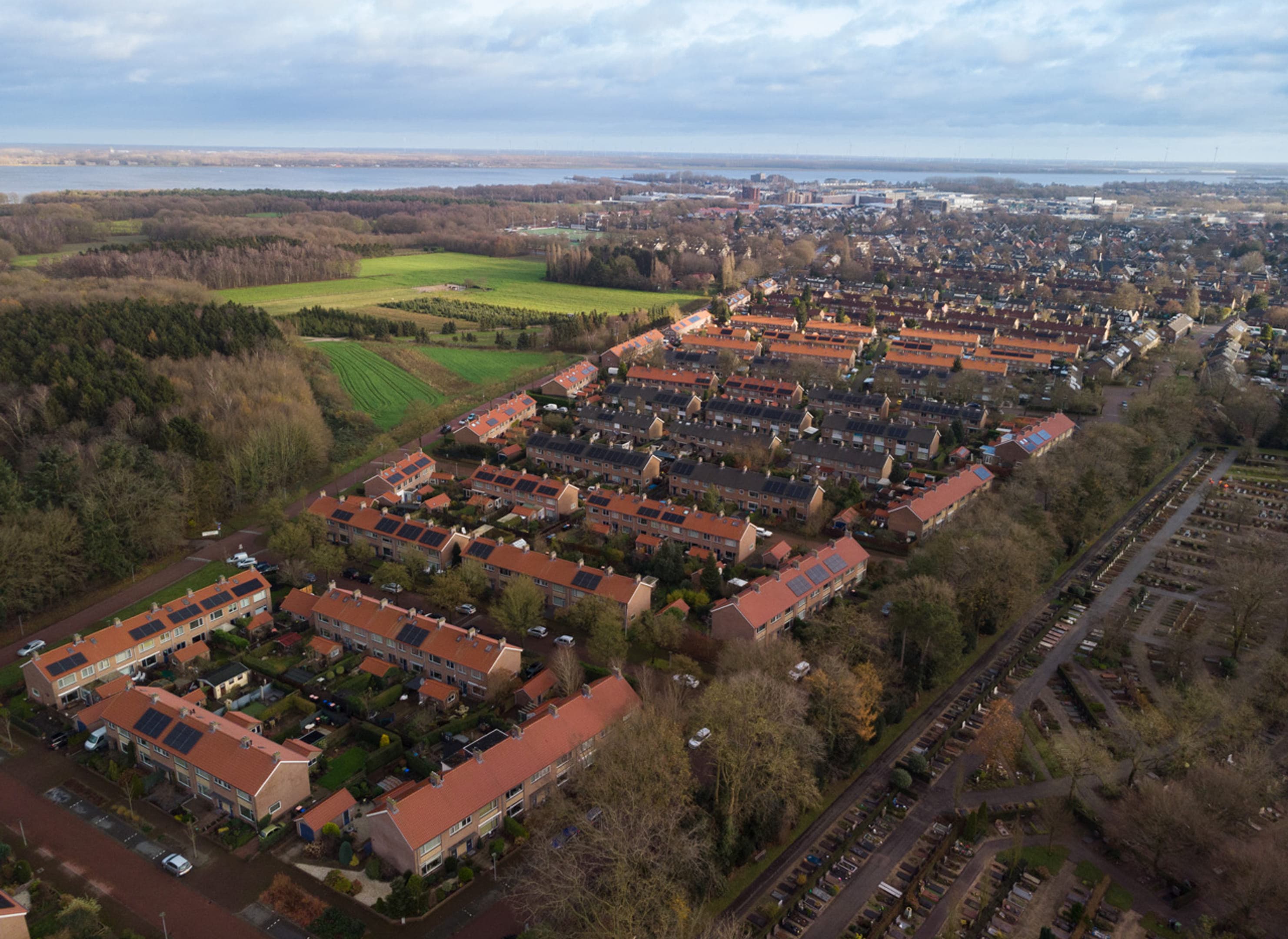 Dronebeeld van een woonwijk met rijtjeshuizen, park en water op de achtergrond