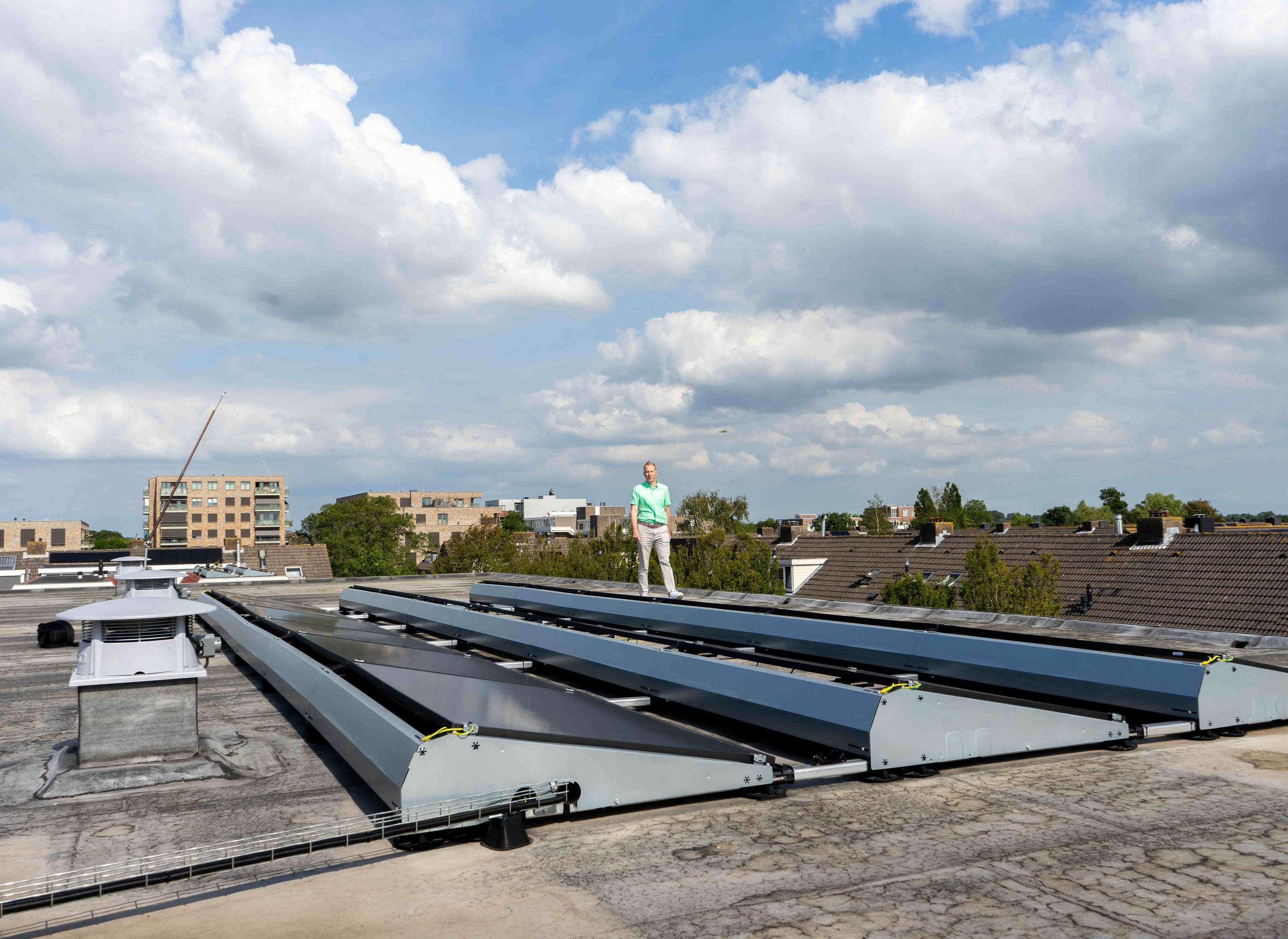 Man op het dak van een flatgebouw naast drie rijen zonnepanelen